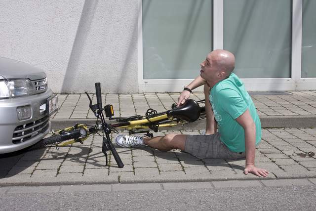 Bicyclist on pavement next to bike with GEICO behind him