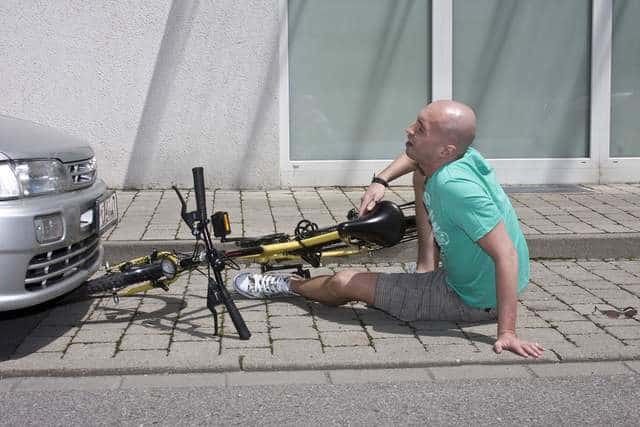 Bicyclist on pavement next to bike with GEICO behind him