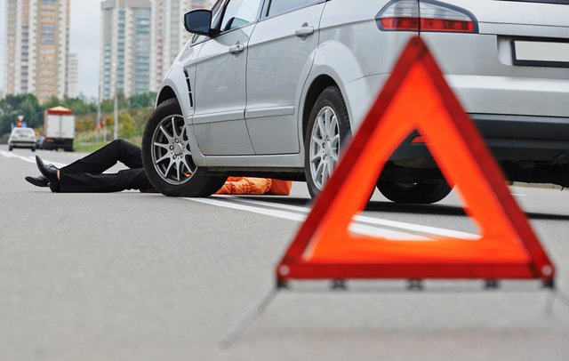 Pedestrian lying on road. in front of car that is stopped. Red warning triangle behind car.
