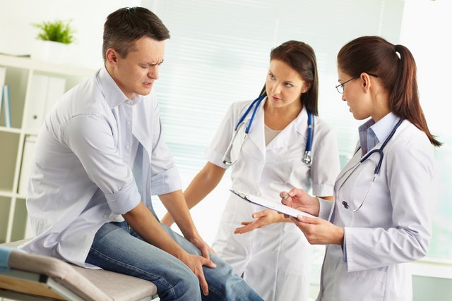 Man in pain holding knee. Doctor and nurse examining him. 