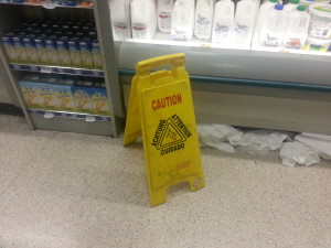 Yellow Caution Warning Sign Paper towels on floor next to refrigerator containing milk in supermarket