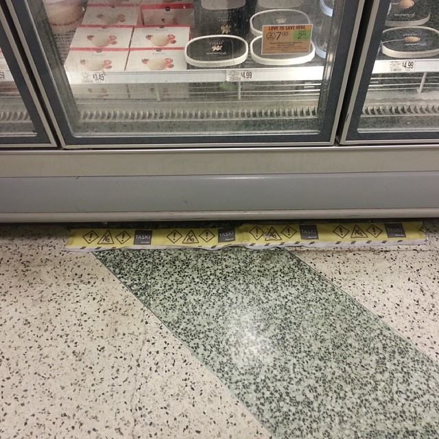 Yellow caution pad in front of commercial freezer at supermarket to warn shoppers and soak up water and prevent slip and falls