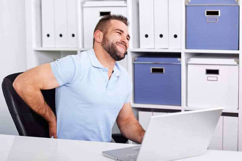 Man holding lower back in pain at desk in office. 