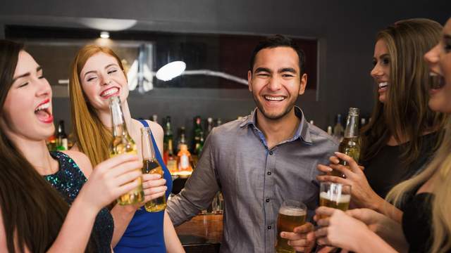 Man at bar smiling and drinking beer with four women.