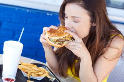 Woman eating cheeseburger, fries and drinking at restaurant.