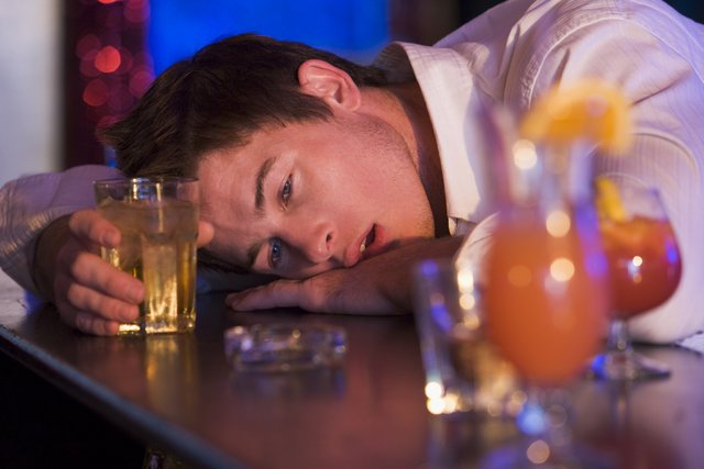 Drunk young man at bar holding glass of liquor.