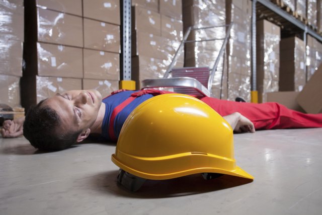 Employee laying on floor at warehouse. Hat fell off and is neck to him.