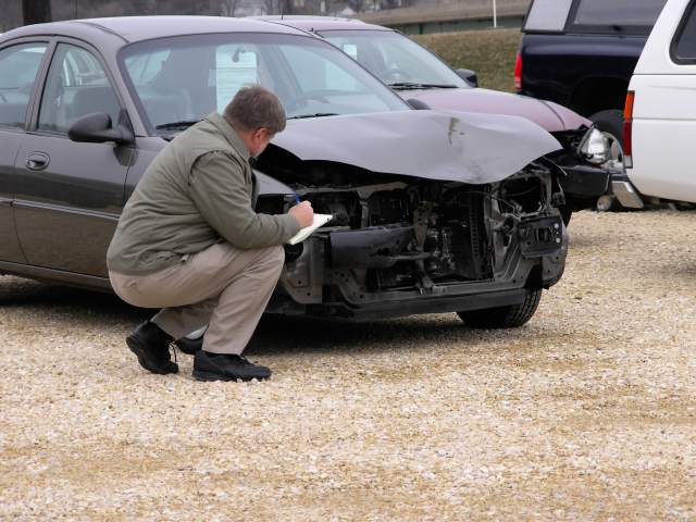 Insurance claim adjuster inspects front of vehicle